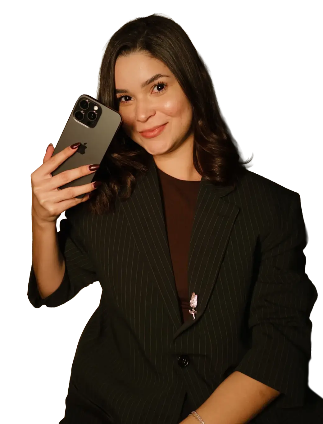 Pâmella Machado sorrindo, de blazer risca-de-giz, com o iPhone encostado no rosto.